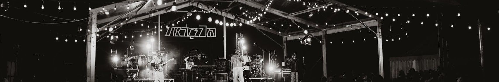 The Handawaka band performing on stage under a canopy of string lights, in black and white